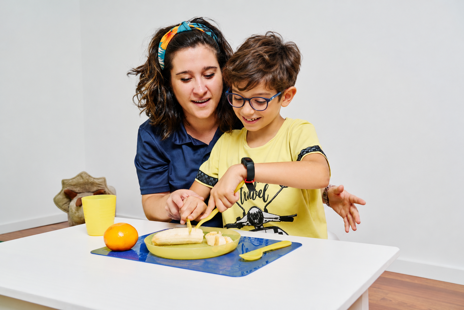 Terapeuta ocupacional acompaña a un niño durante una actividad de preparación de alimentos con cubiertos.